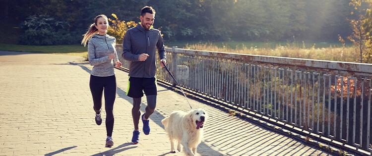 Dos personas corriendo con un perro con correa.