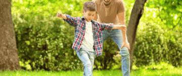 Photo of a young father playing soccer with his son at a park